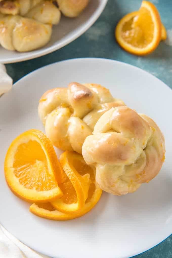 two knotted orange sweet rolls with orange slices on a white plate