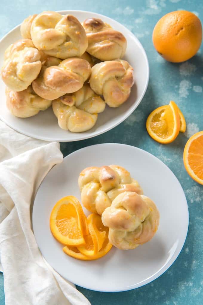 white plates of orange sweet knot rolls and sliced oranges
