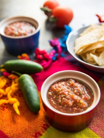 a bowl of mexican resaurant style salsa next to peppers and chips