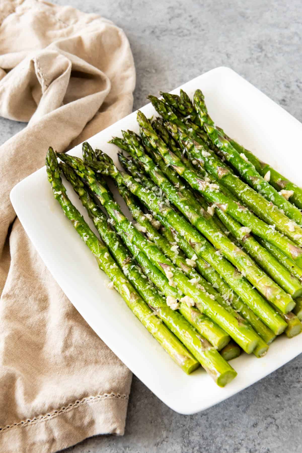 A white plate with a pile of neatly stacked asparagus over a tan tea towel.