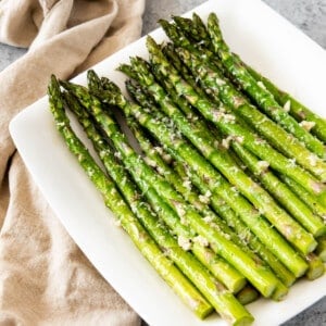 A pile of neatly arranged asparagus on a white square plate.