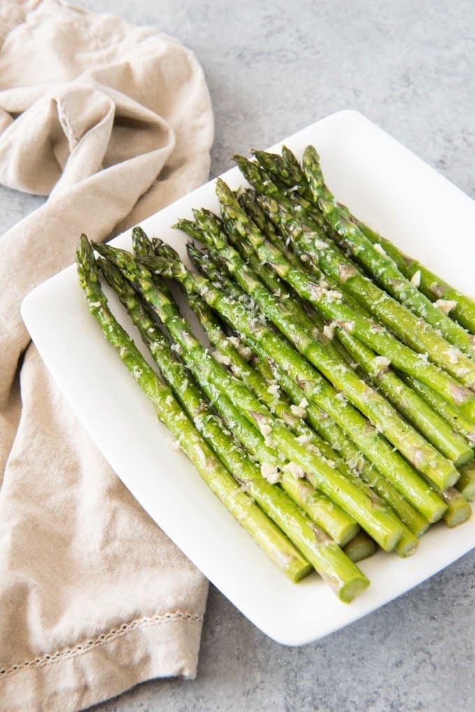 a white plate with a pile of neatly stacked asparagus over a tan tea towel
