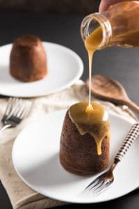 Sticky Toffee Pudding Cake with toffee being poured out of a bottle onto the towering food