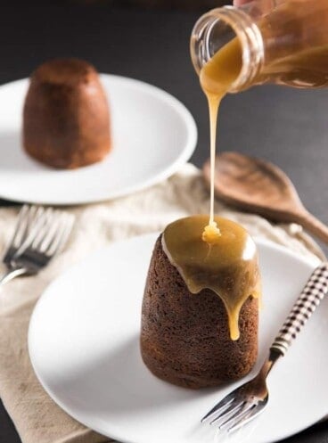 Sticky Toffee Pudding Cake with toffee being poured out of a bottle onto the towering food