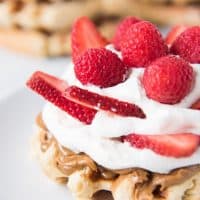 waffle topped with cream and fresh berries with more waffles in the background