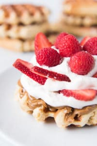 waffle topped with cream and fresh berries with more waffles in the background