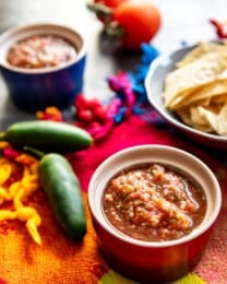 A bowl of Mexican restaurant style salsa next to peppers and chips.