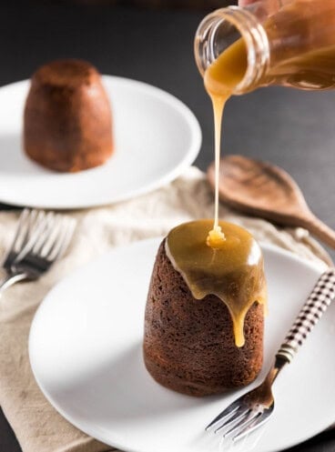 Sticky Toffee Pudding Cake with toffee being poured out of a bottle onto the towering food