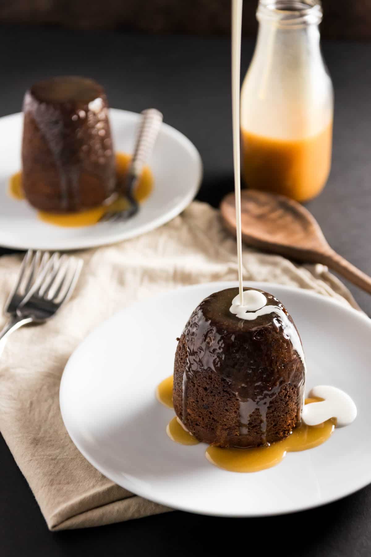 pouring a drizzle of heavy cream over sticky toffee pudding