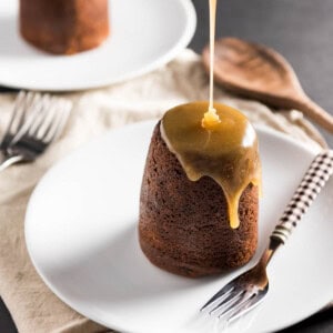 Sticky Toffee Pudding Cake with toffee being poured out of a bottle onto the towering food