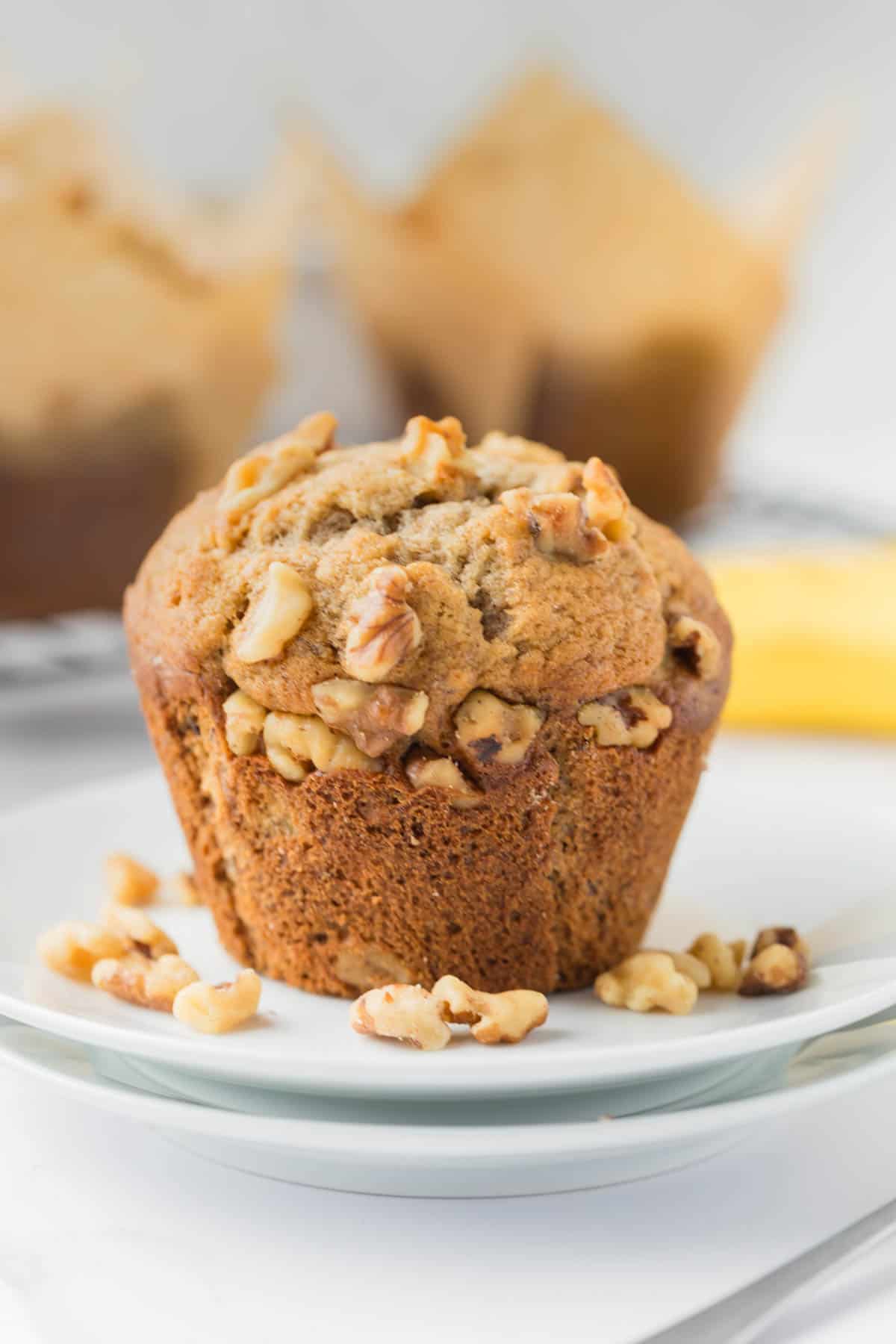 An image of a banana nut muffin on a plate with chopped walnuts.