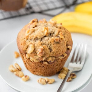 An image of a banana nut muffin on a white plate with a fork.