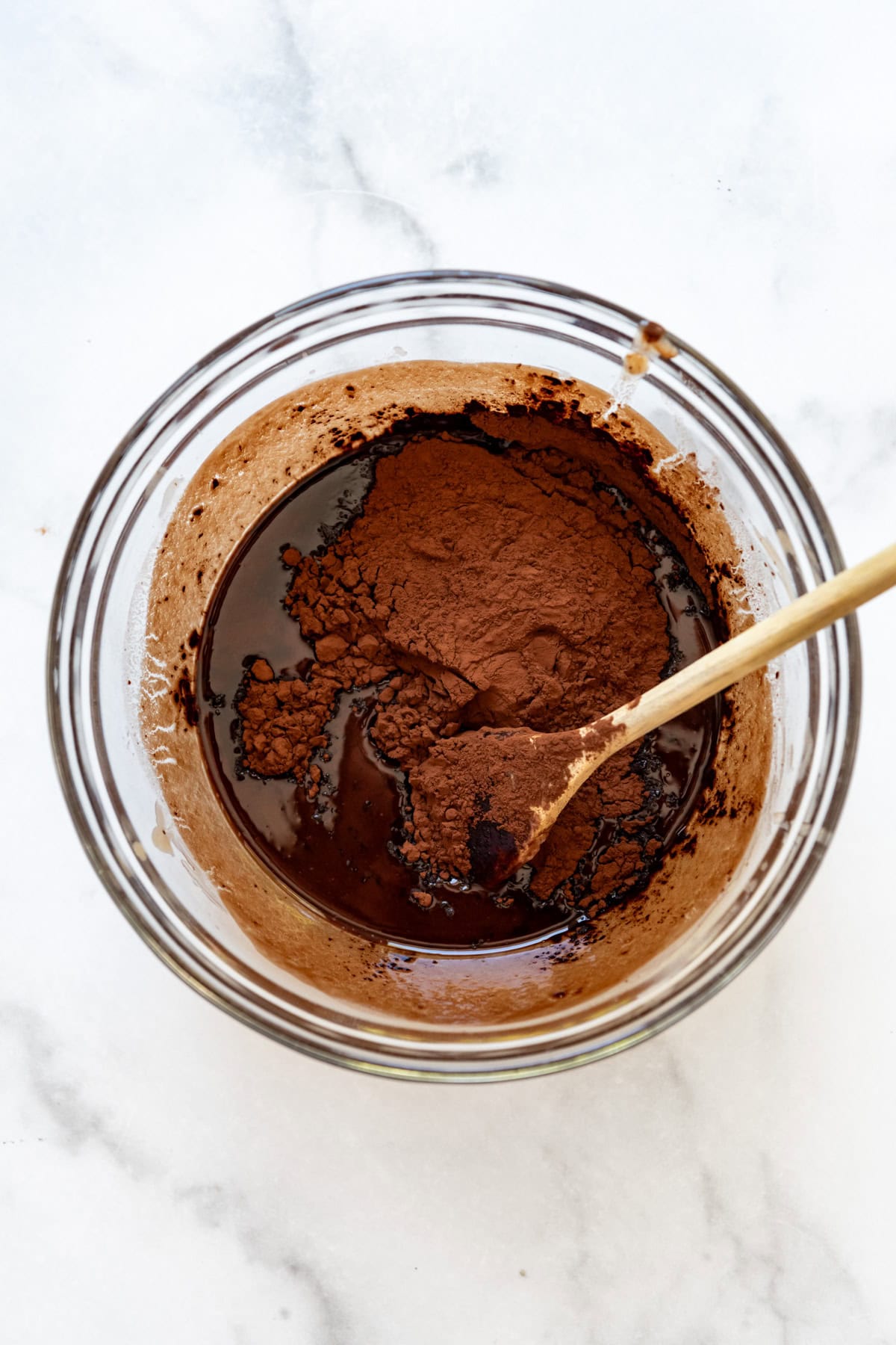 Adding cocoa powder to melted butter and chocolate in a bowl.