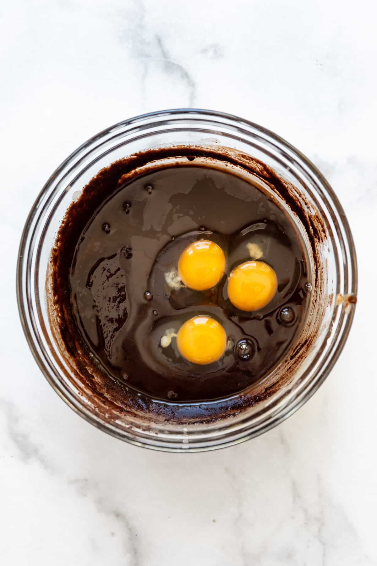 Adding eggs and vanilla to brownie batter in a bowl.