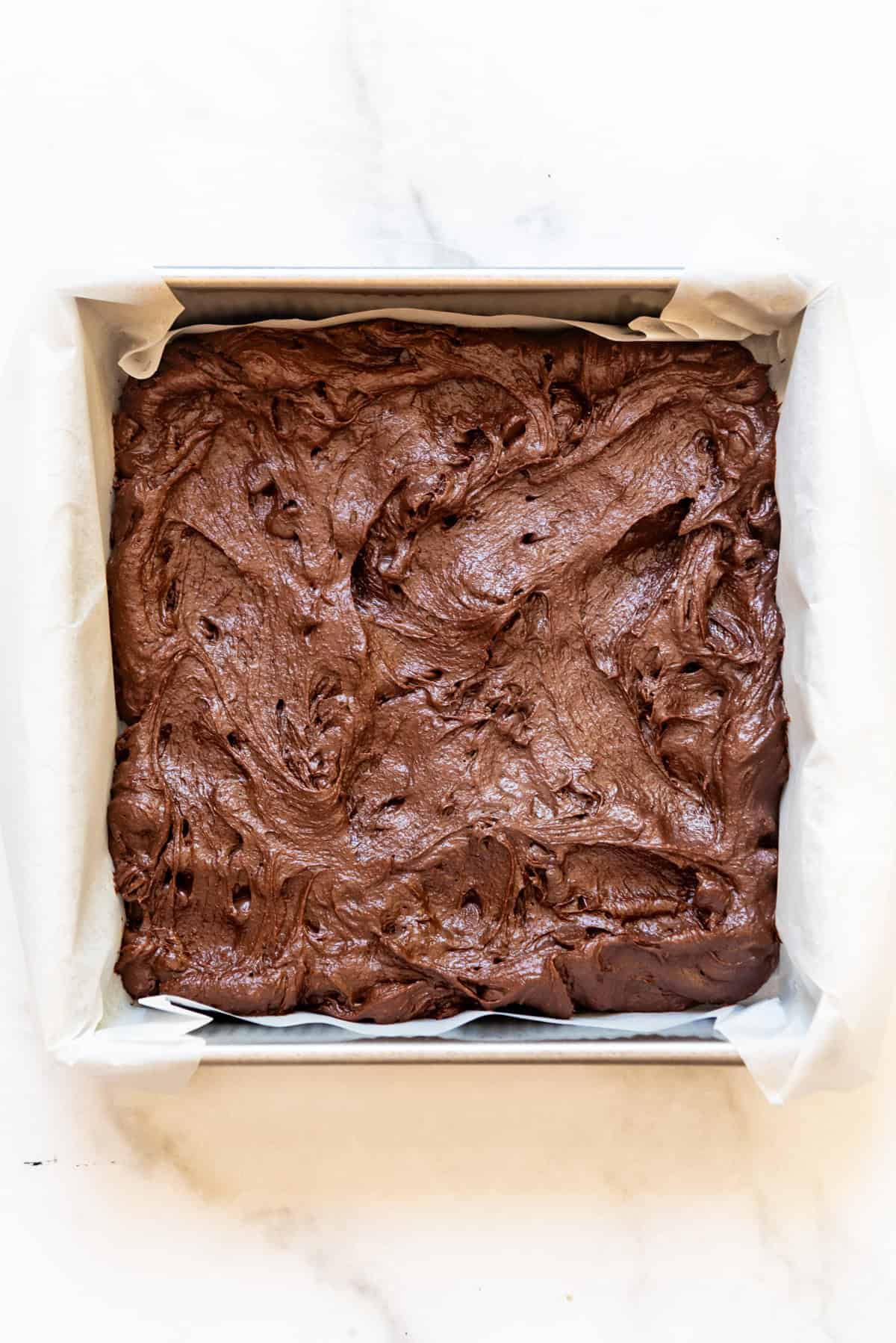 Brownie batter in a pan lined with parchment paper.