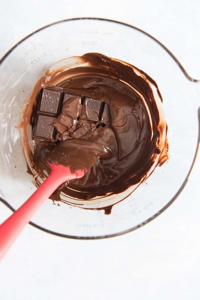 a bowl with melted chocolate and a chocolate bar and rubber spatula