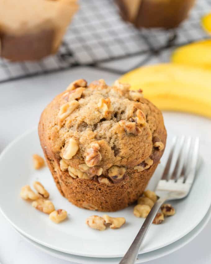 An image of a banana nut muffin on a plate with chopped walnuts.