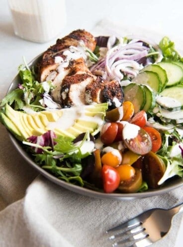 Grilled Cajun Chicken Salad ingredients all in a bowl with dressing drizzled over the top