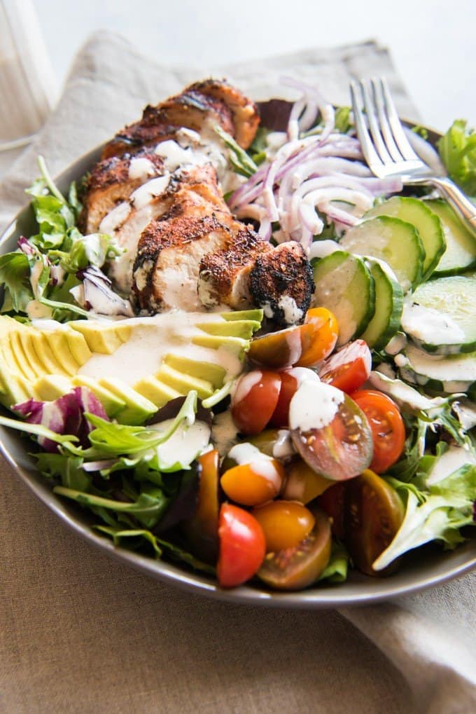grilled cajun chicken salad ingredients and dressing all in a bowl with a fork