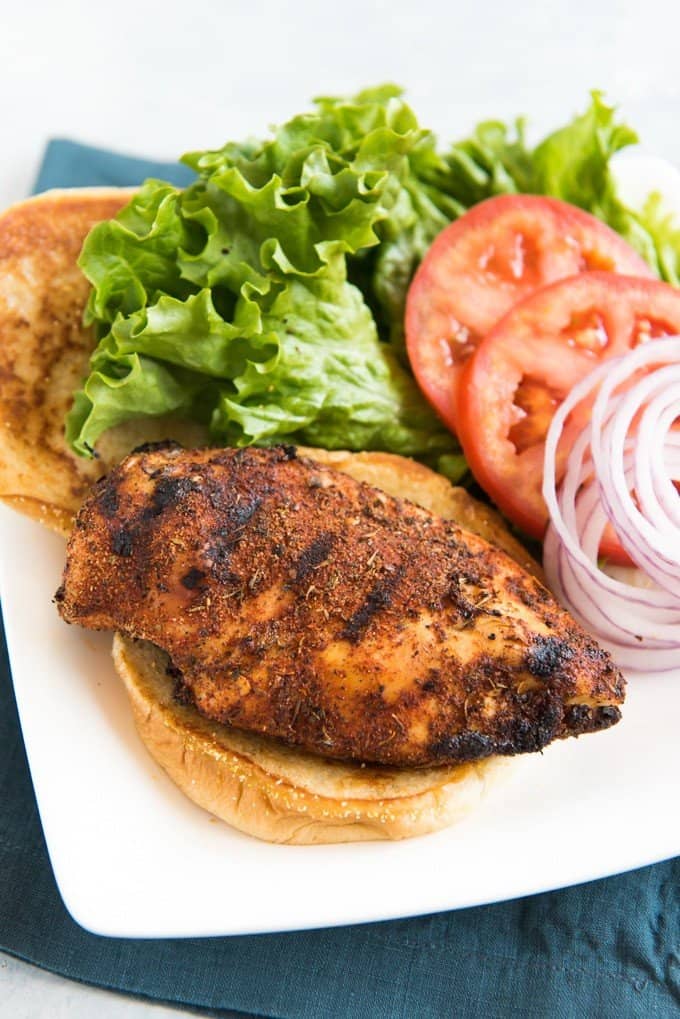 grilled chicken on a burger bun with lettuce tomatos and sliced red onions