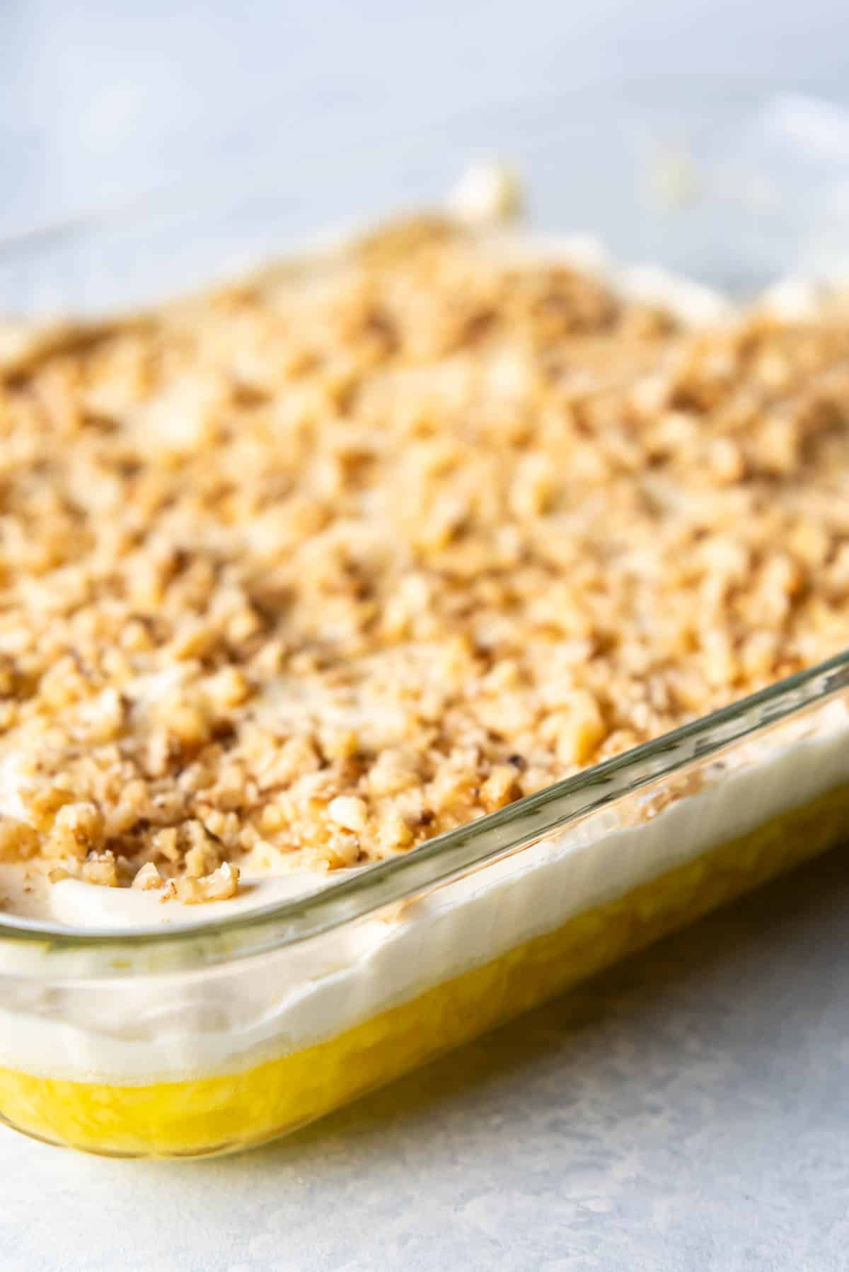 A side view of a lemon pineapple jello with whipped cream and chopped walnuts.