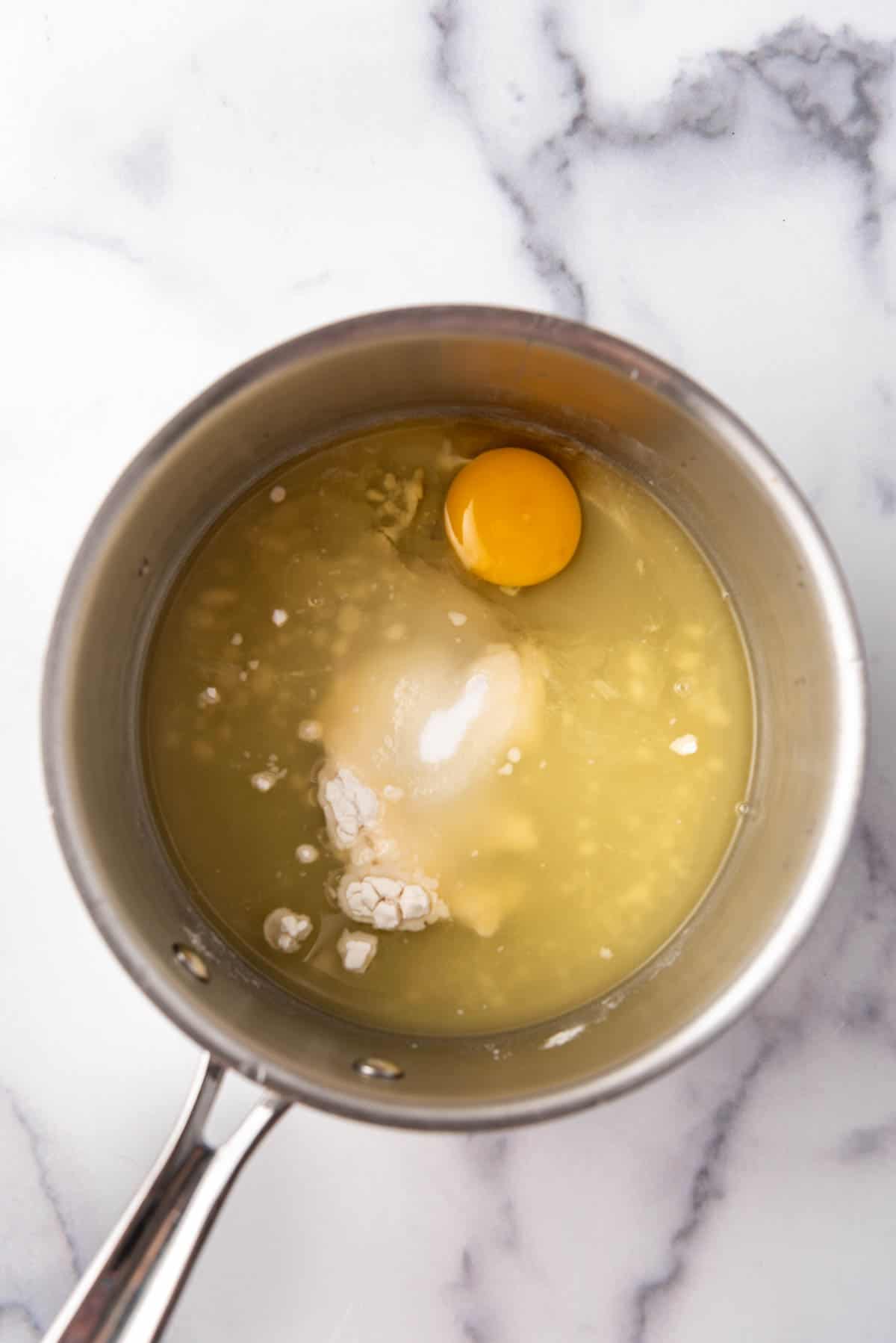 Combining pineapple juice, flour, sugar, and an egg in a saucepan.