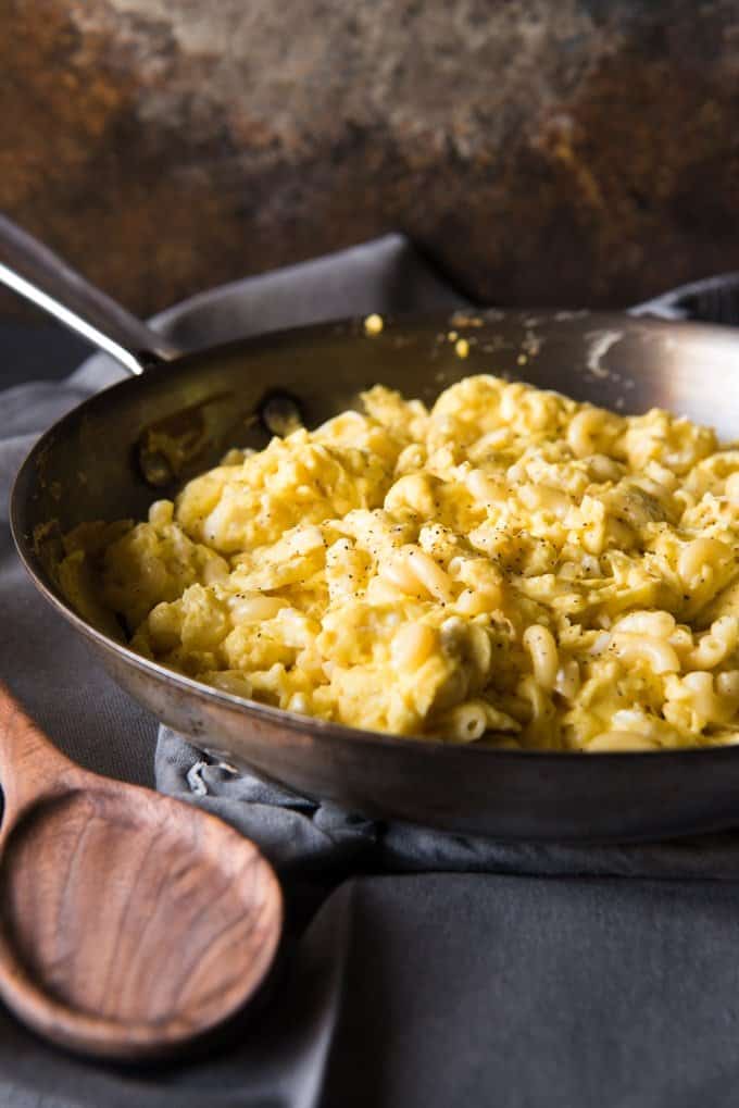 a skillet with peppery macaroni eggs inside and a wooden spoon off to the side