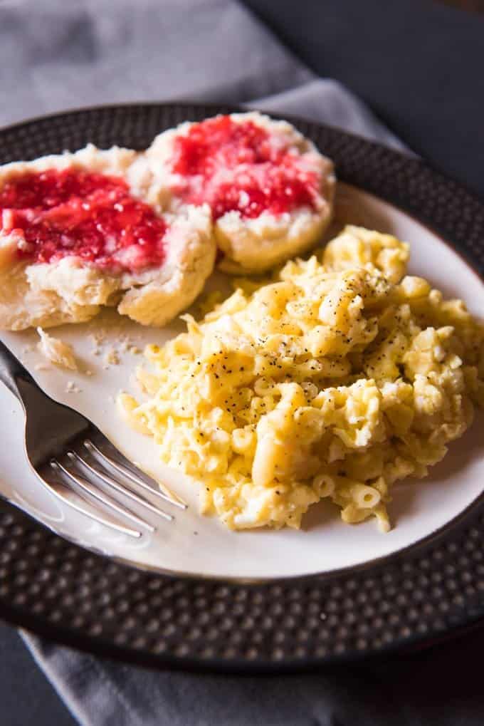 peppery scrambled macaroni eggs on a plate with a fork and jam covered biscuit