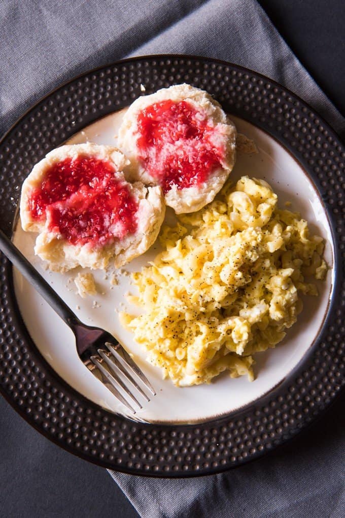 A plate with pink jam covered biscuits a fork and scrambled egg macaroni