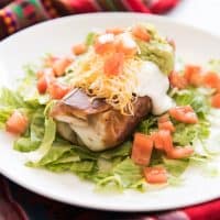 a Chimichangas on a bed of lettuce on a white plate topped with sour cream, guac, tomatoes, and cheese