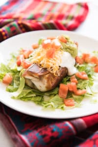 a Chimichangas on a bed of lettuce on a white plate topped with sour cream, guac, tomatoes, and cheese