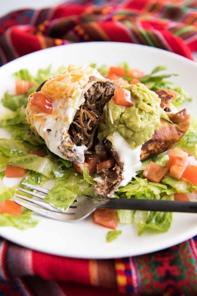 a shredded beef chimichanga with lettuce tomato guacamole and sour cream