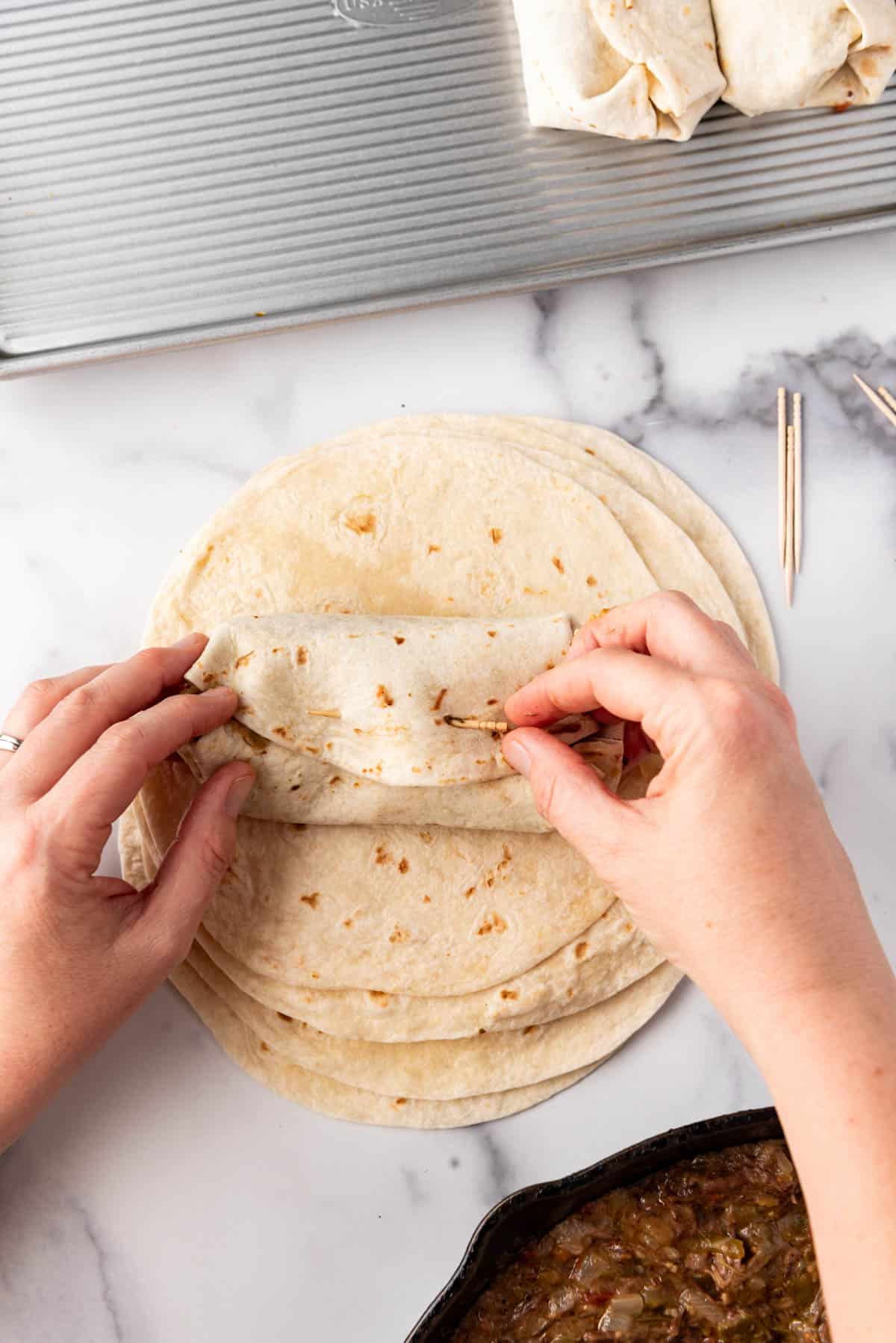 Securing a chimichanga with a toothpick before frying.