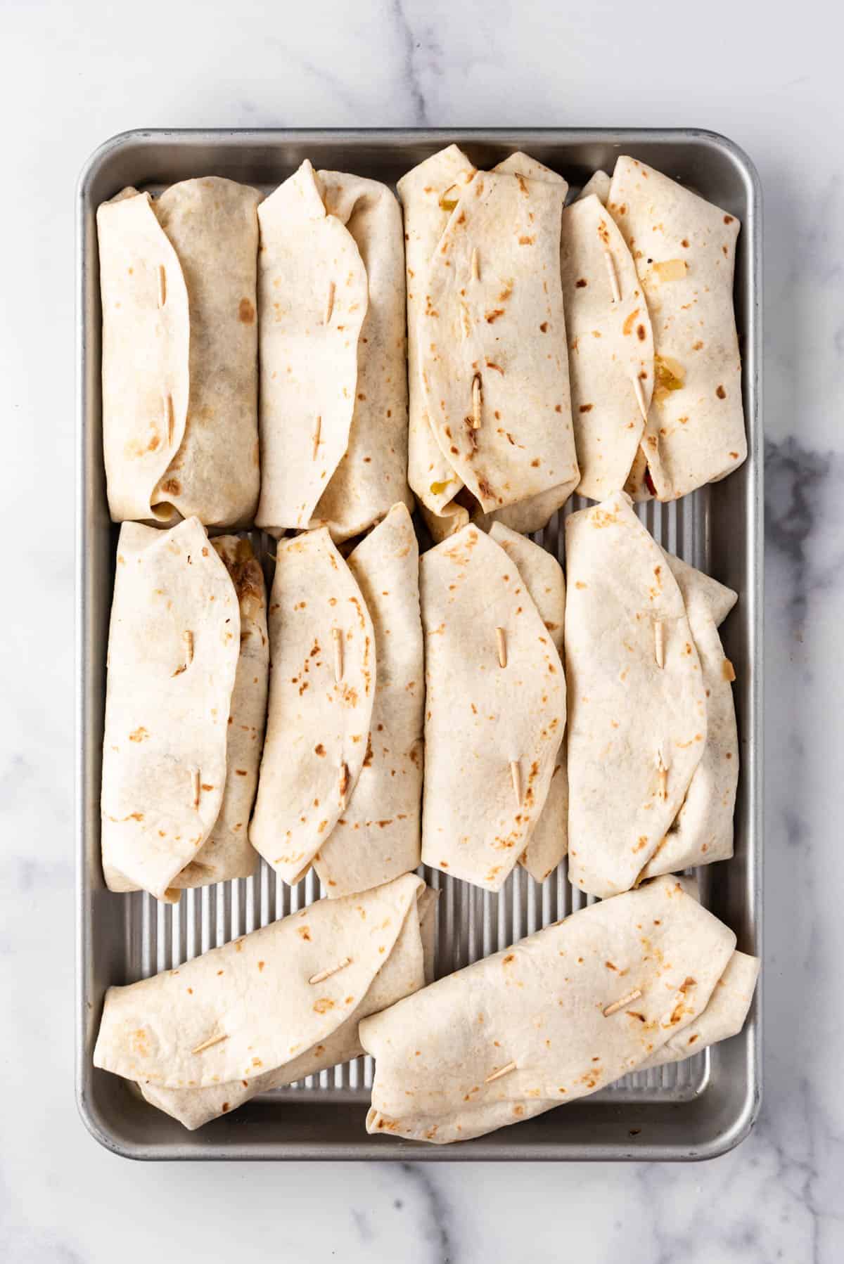 An overhead image of assembled chimichangas on a baking sheet before frying.