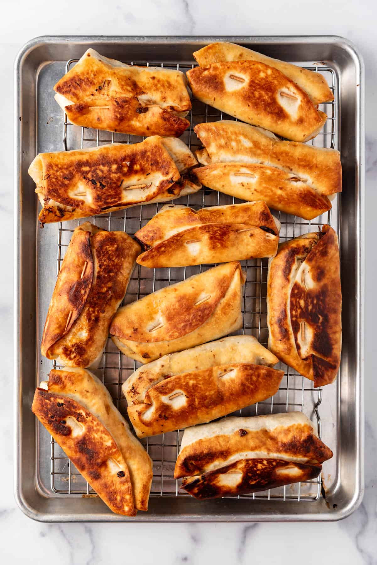 An overhead image of cooked chimichangas draining on a wire rack.