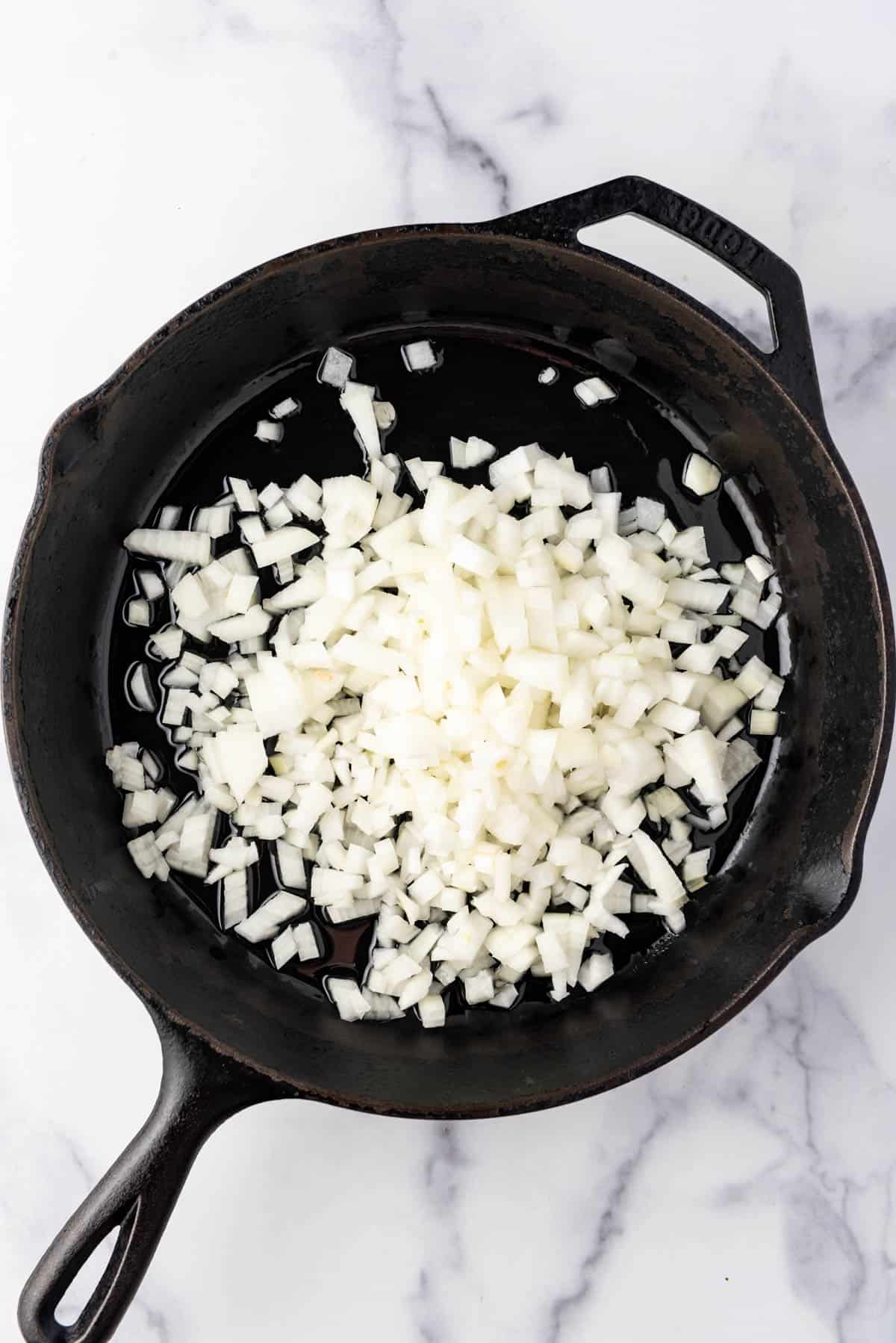 Sauteeing chopped onions in a large cast iron skillet.