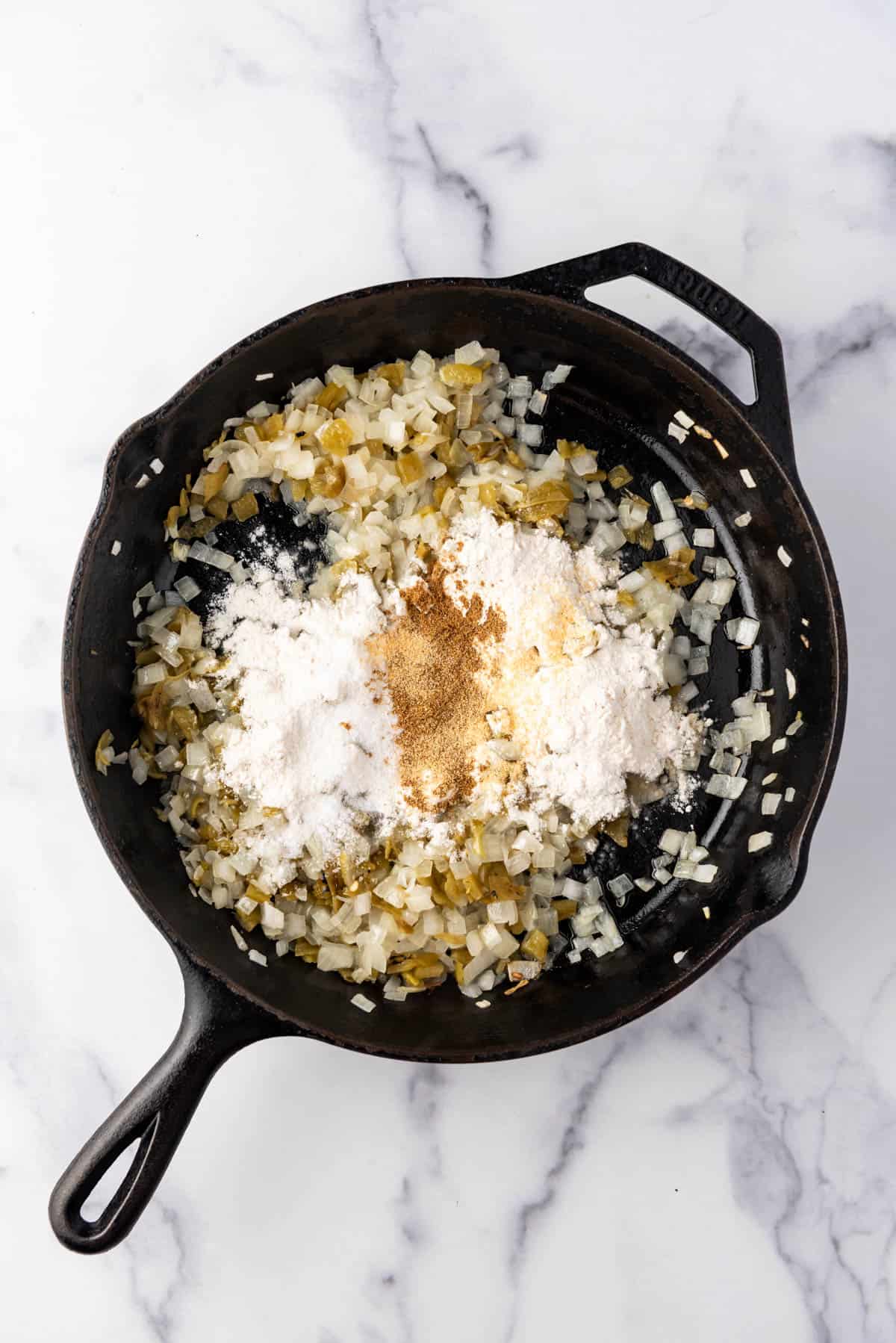 Adding flour and spices to cooked onions and chili peppers in a pan.