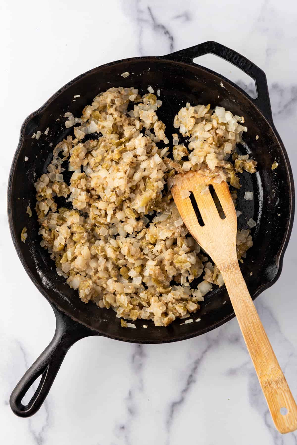 Cooked vegetables in a cast iron skillet with a wooden spatula.