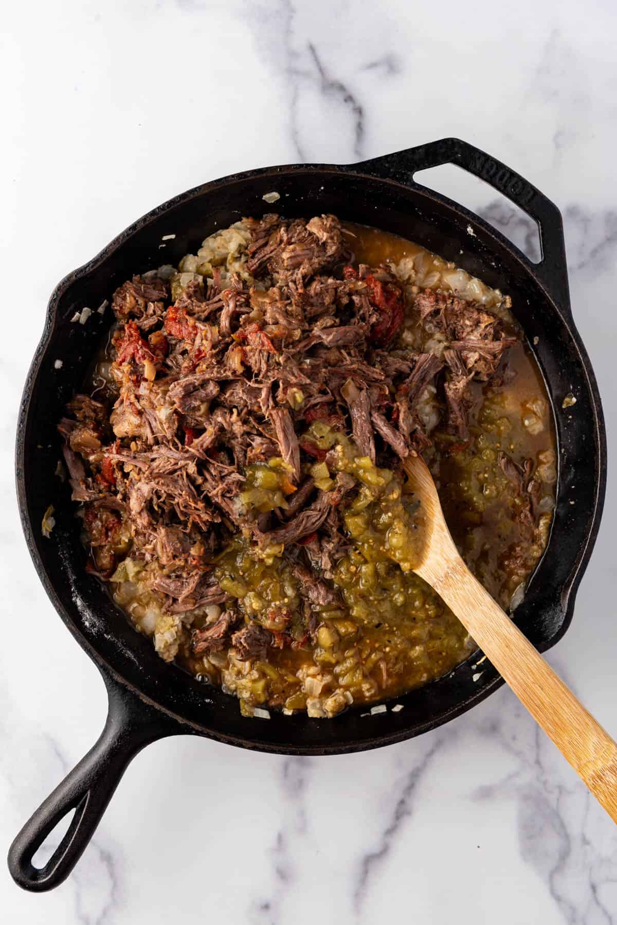 An overhead image of shredded beef chimichangas filling in a cast iron skillet.