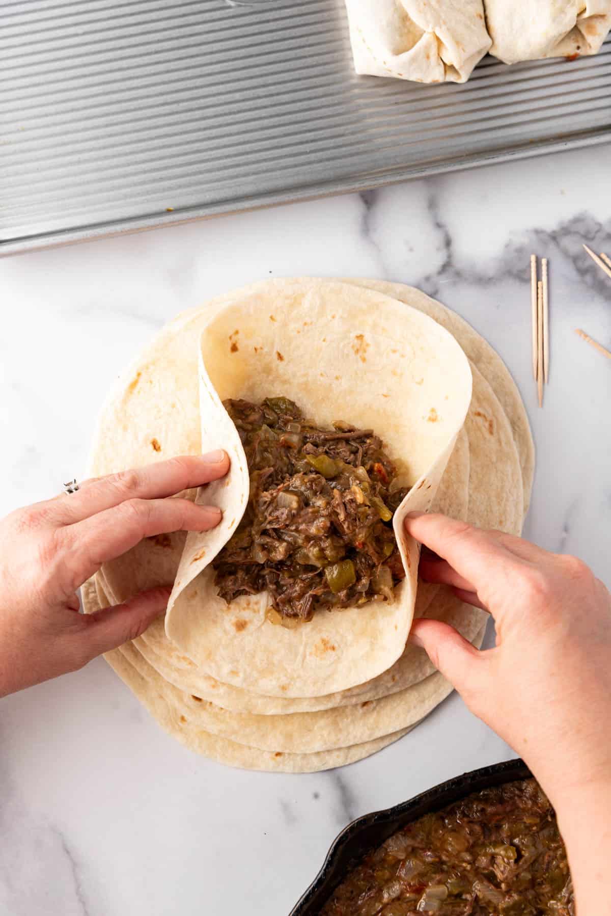 Hands folding a tortilla around shredded beef filling.