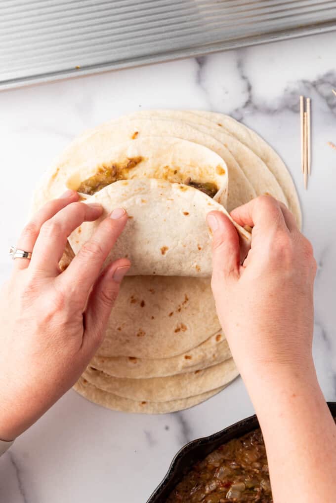 Hands folding a tortilla around beef filling for a chimichanga.