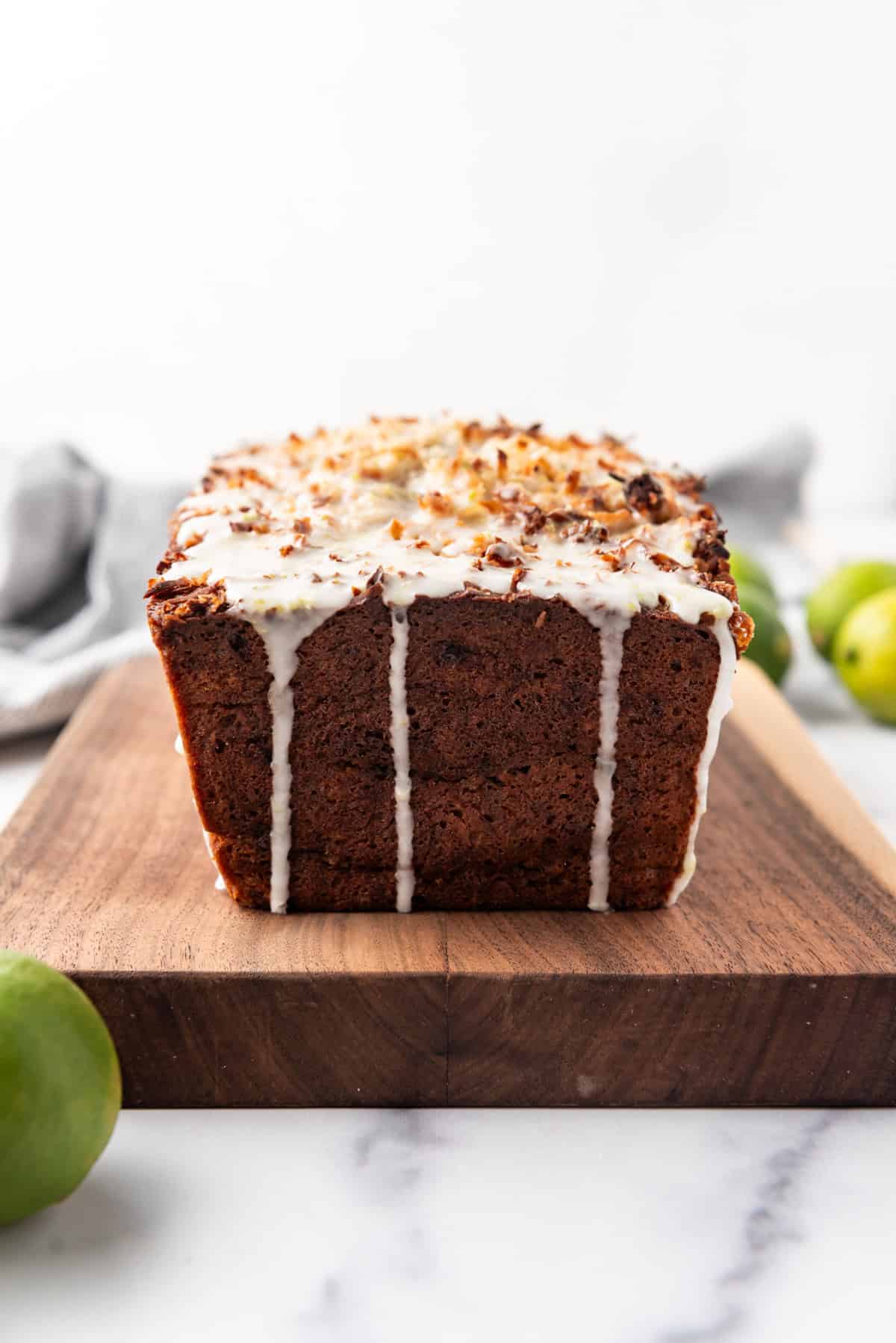 A loaf of coconut lime glazed banana bread on a wooden cutting board.