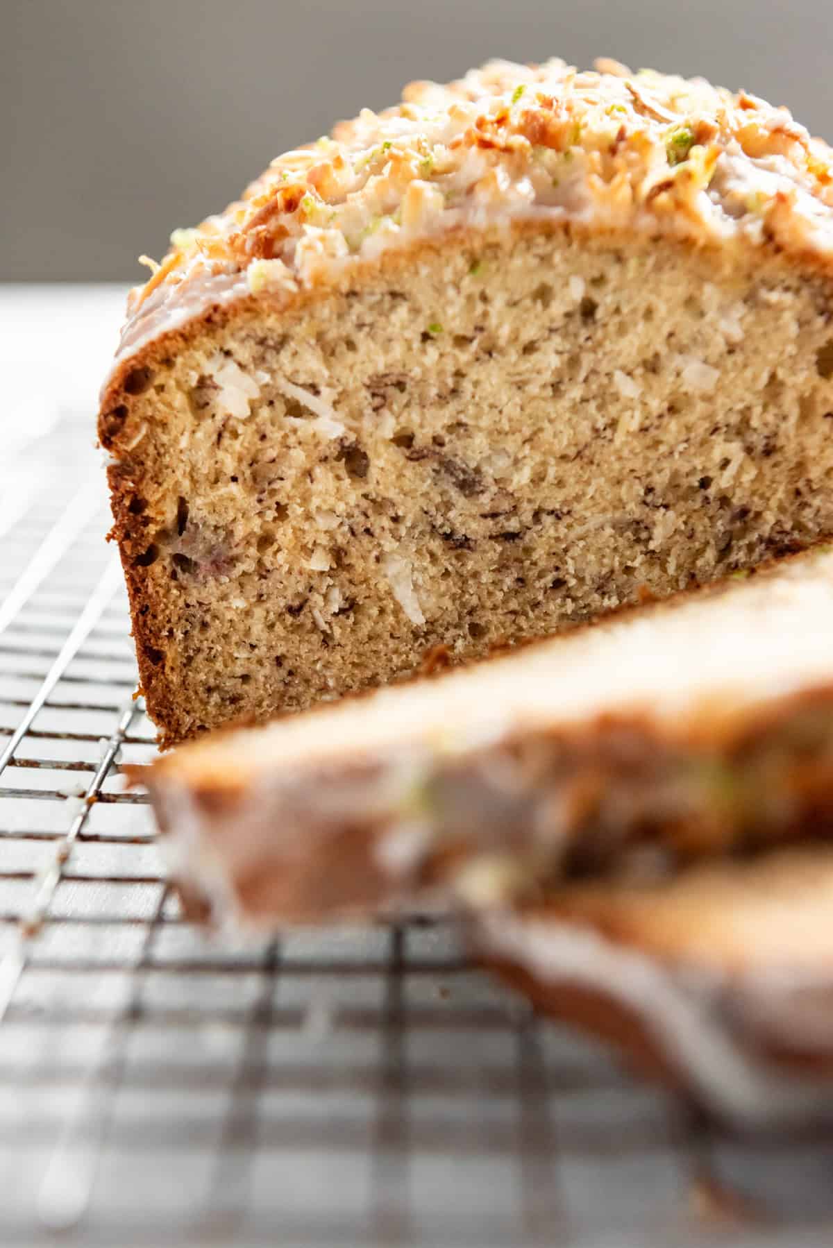 a sliced loaf of Coconut Lime Glazed Banana Bread on a wire rack