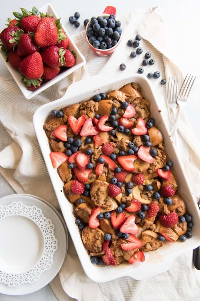 a white baking dish full of berry bagel breakfast casserole with fresh berries to the side