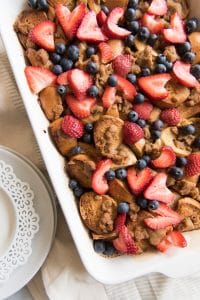 a blueberry and strawberry topped bagel breakfast casserole in a white baking dish