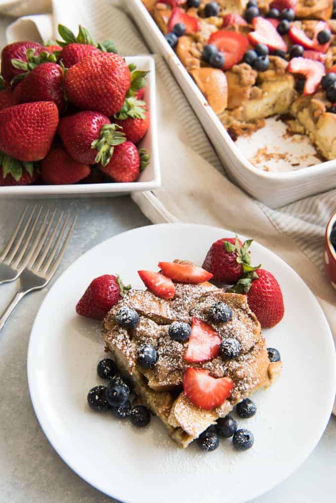 a white plate with berry breakast casserole garnished with powdered sugar