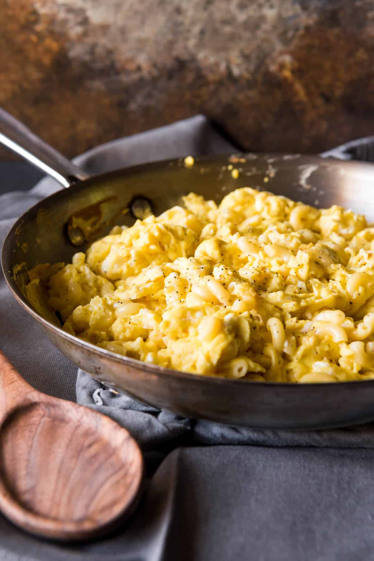 A skillet with peppery macaroni eggs inside and a wooden spoon off to the side.