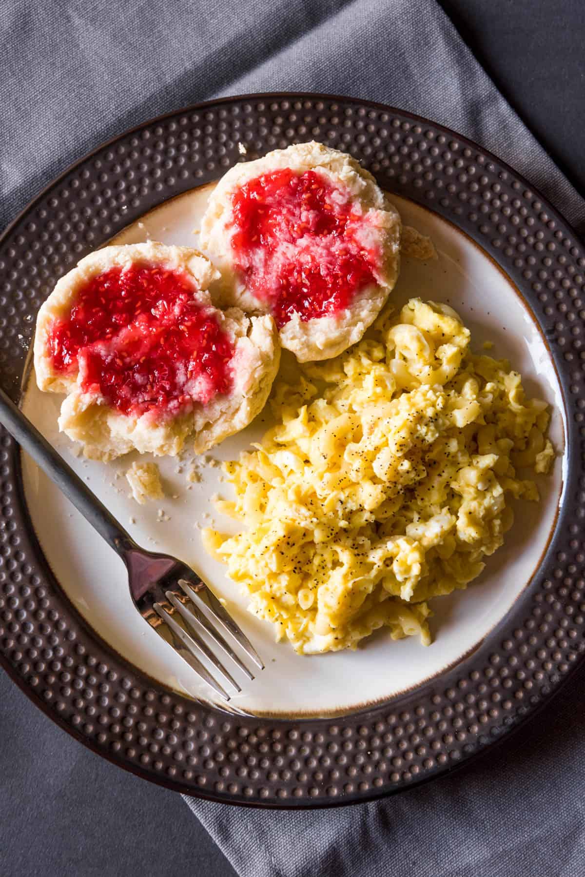 A plate with pink jam covered biscuits a fork and scrambled egg macaroni.