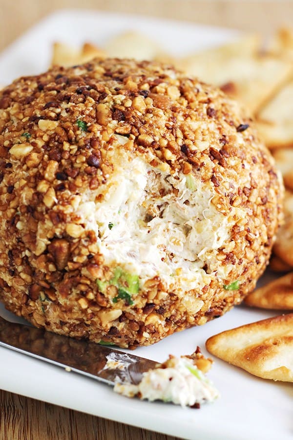 a delicious pina colda cheeseball crusted in nuts and on a white plate with toasted crackers and a spread knife