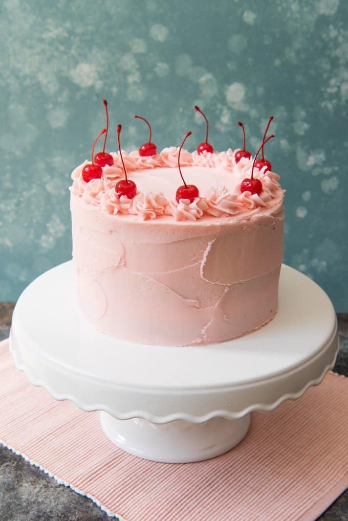 cherry chip cake on a white cake stand with pink frosting and cherries
